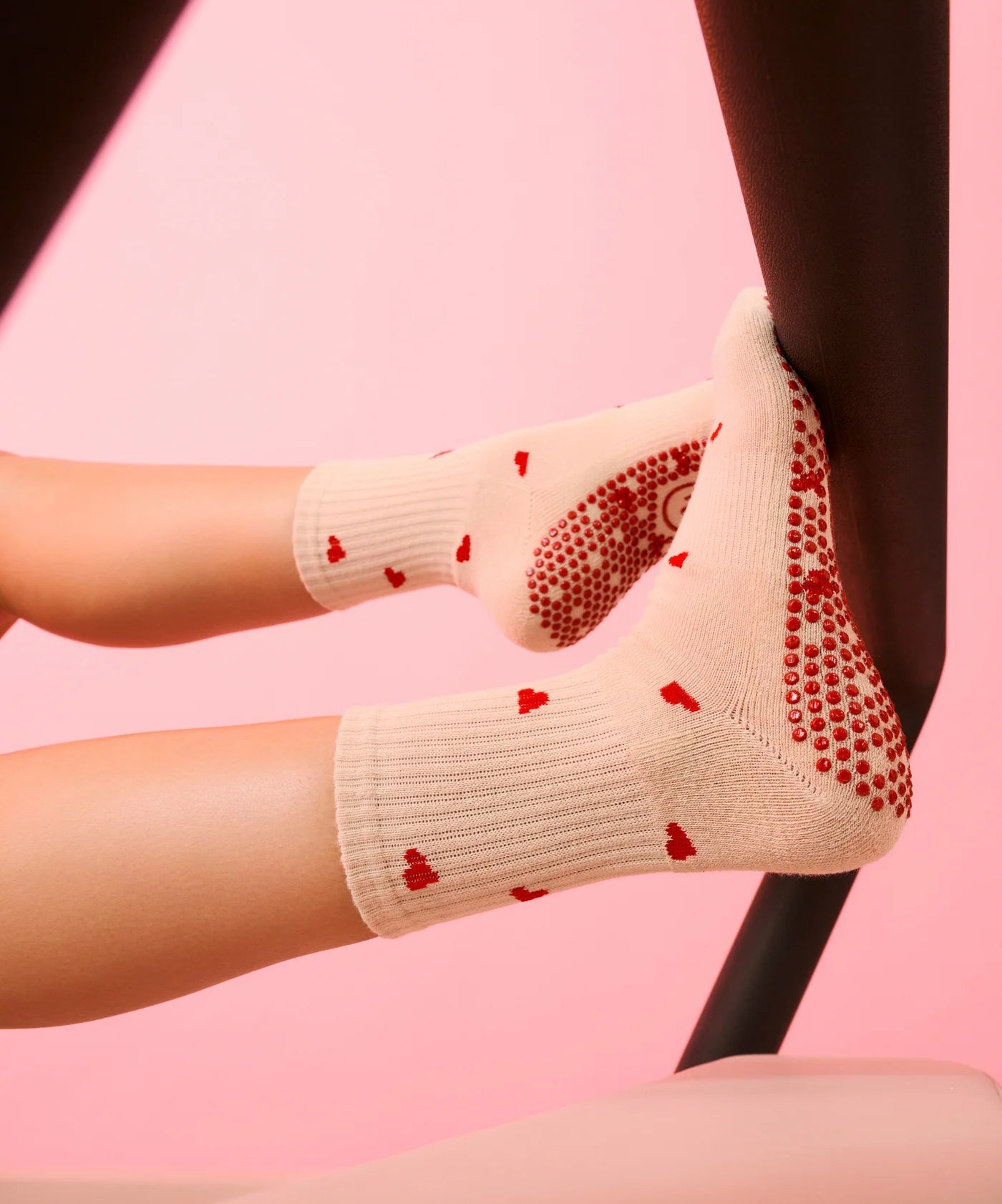 Beige socks with red heart patterns worn by a person on a pink background