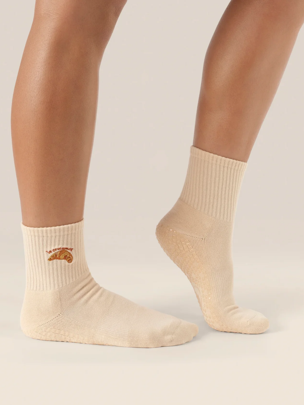 Beige socks with croissant worn by a person on a plain background