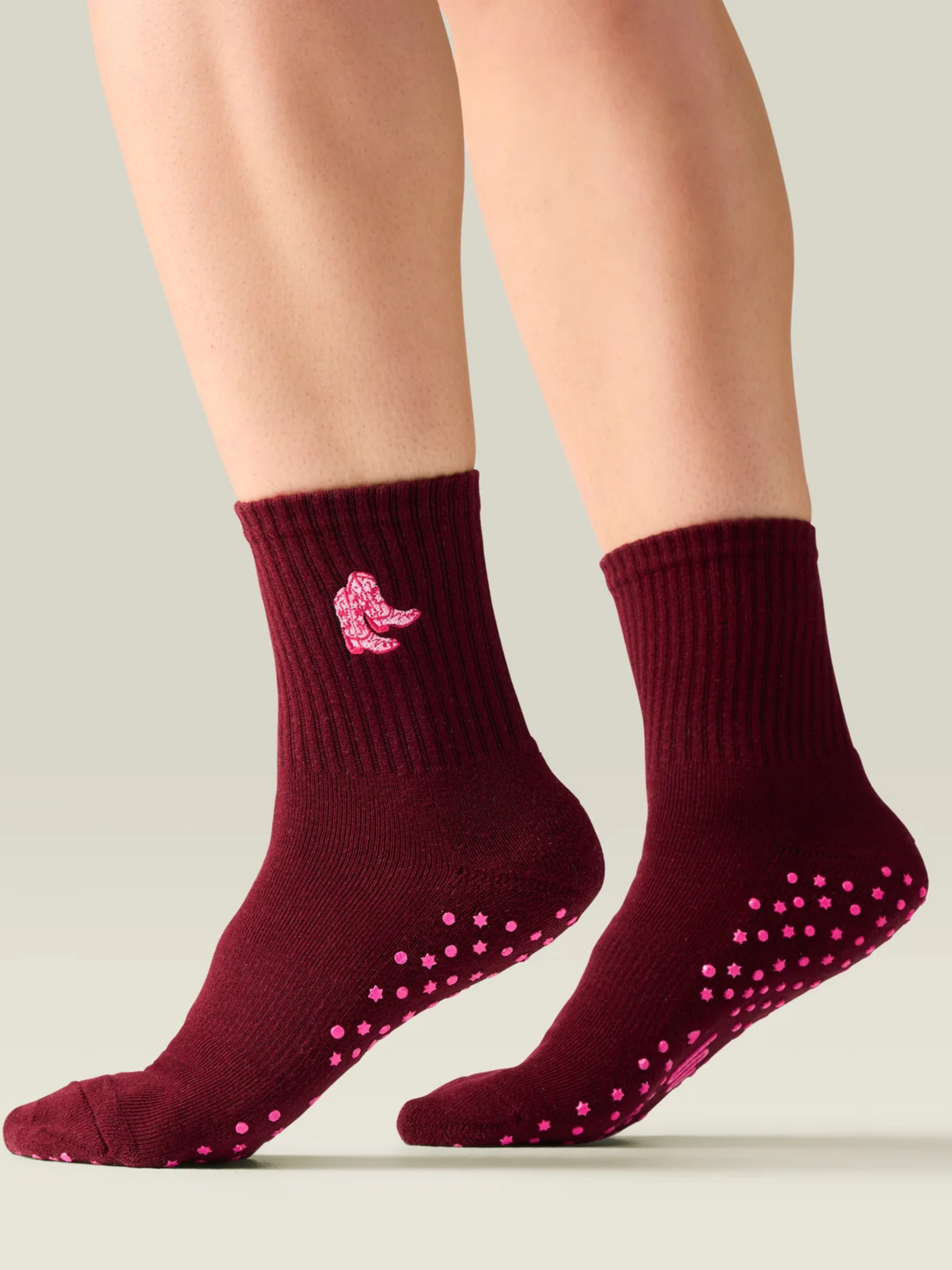 Maroon socks with pink grip dots and a logo on a neutral background