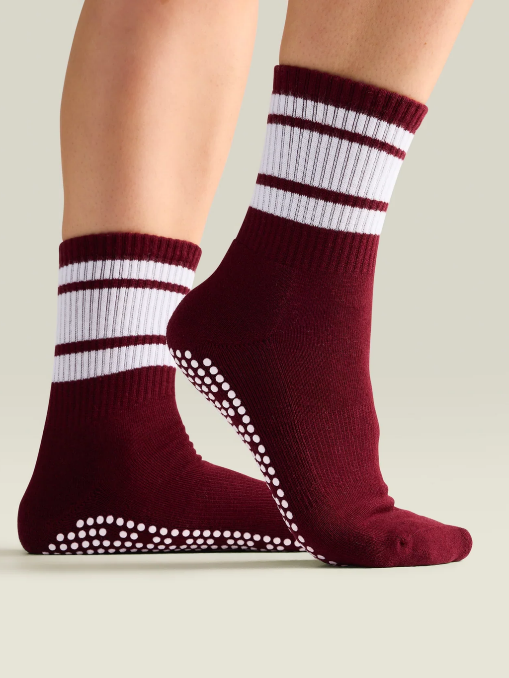 Maroon socks with white stripes and grip dots on a neutral background
