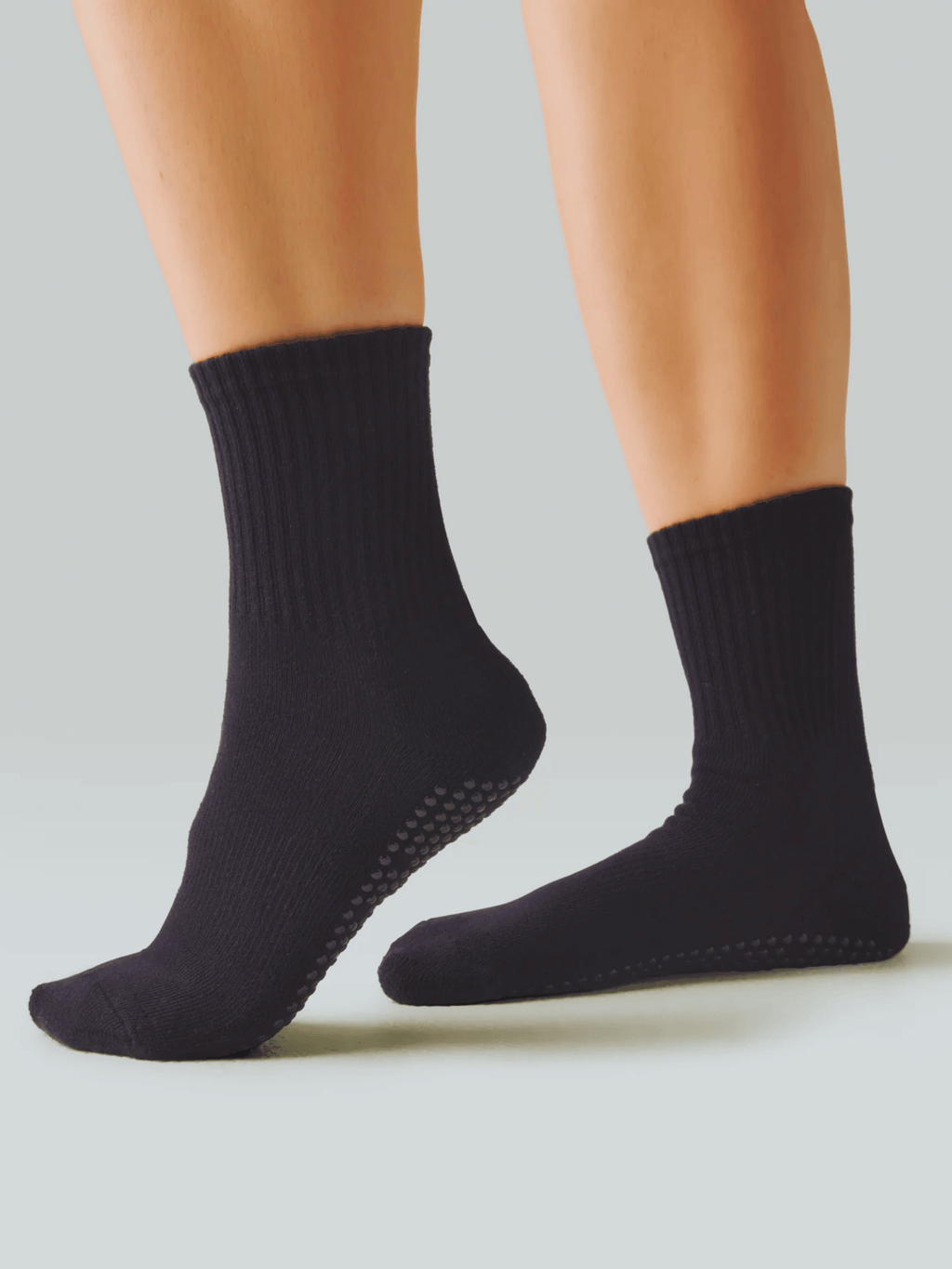 Black socks with non-slip sole worn by a person on a light gray background