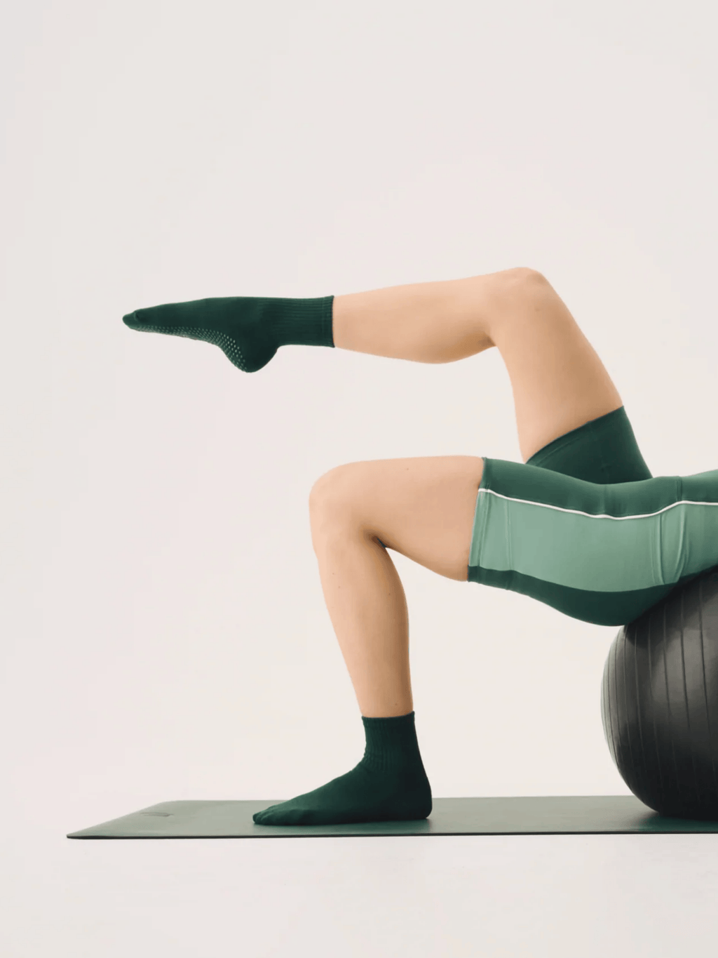 Person exercising on a yoga ball with green socks and leggings against a light background