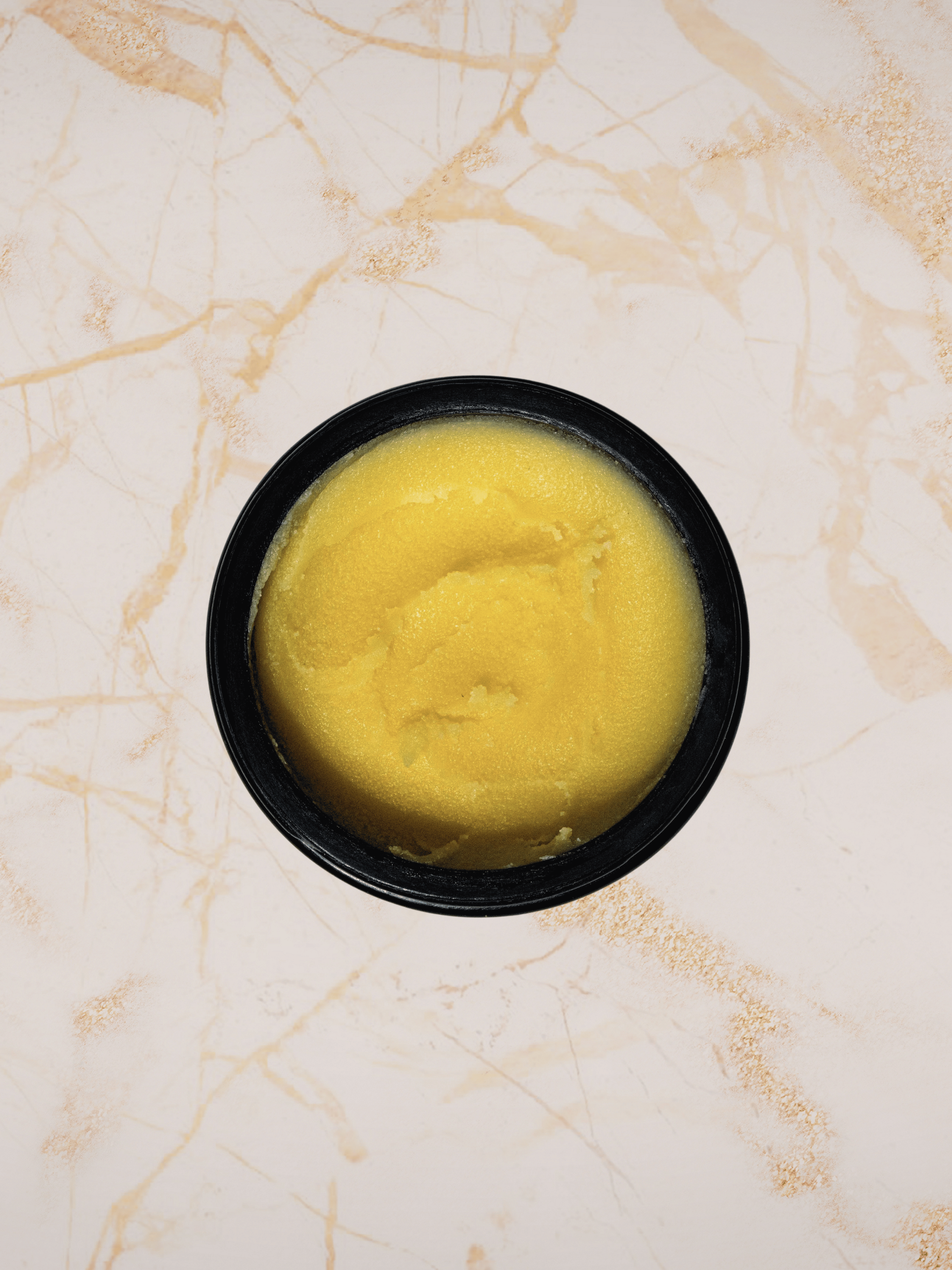 Yellow substance body balm ilapothecary in a black container on a marble surface