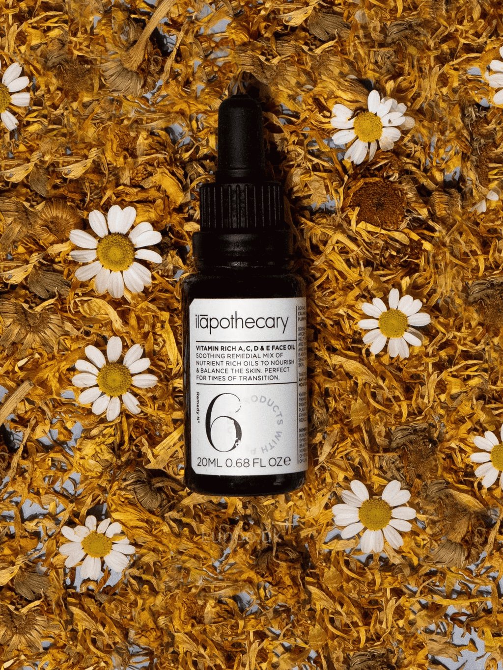 Skincare serum bottle labeled 'vitamin rich a, c, d, e face oil' on a bed of dried flowers and herbs.
