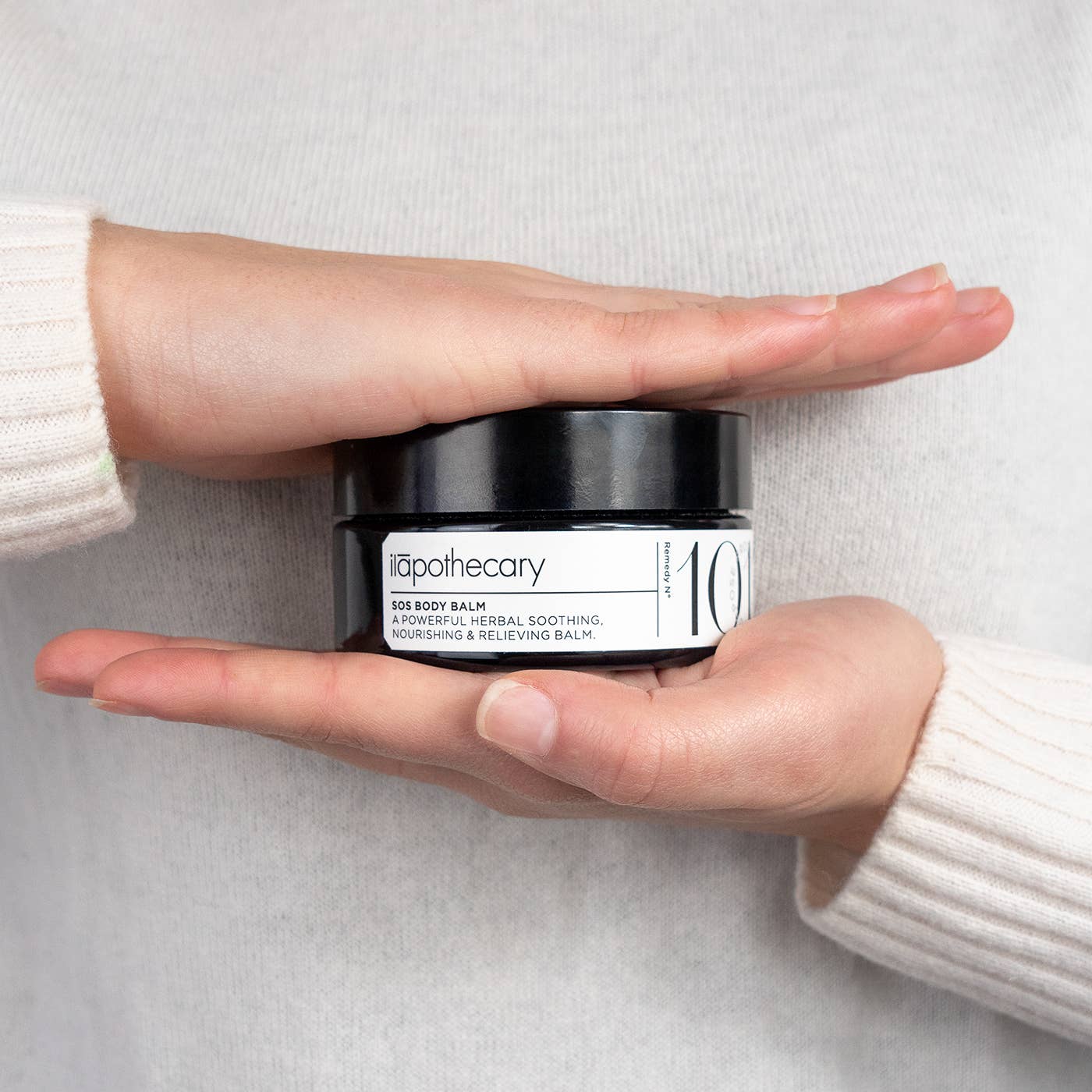 Person holding a jar of itapothecary 10 body balm against a neutral background