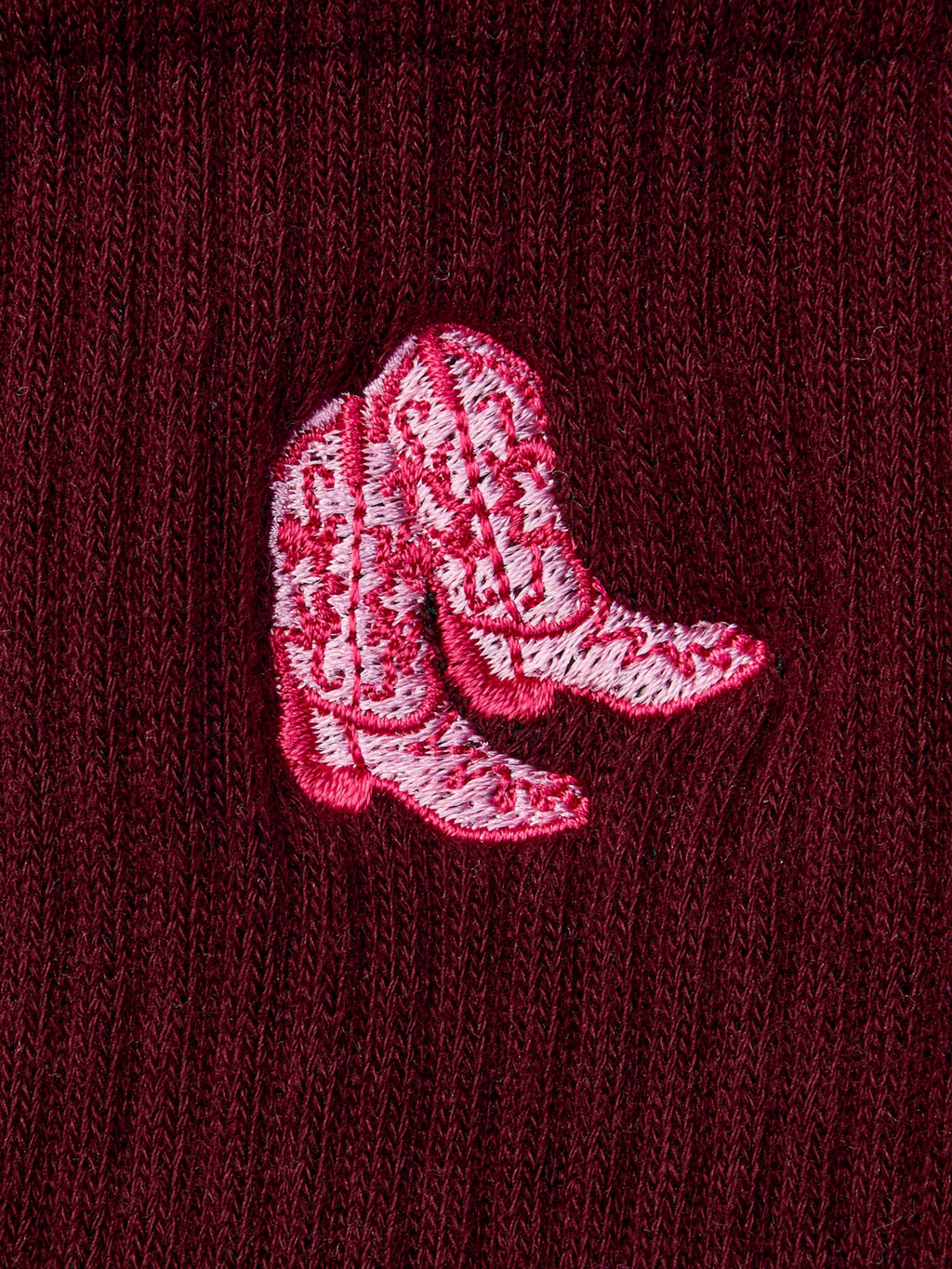 Embroidered pink cowboy boots on a maroon fabric background
