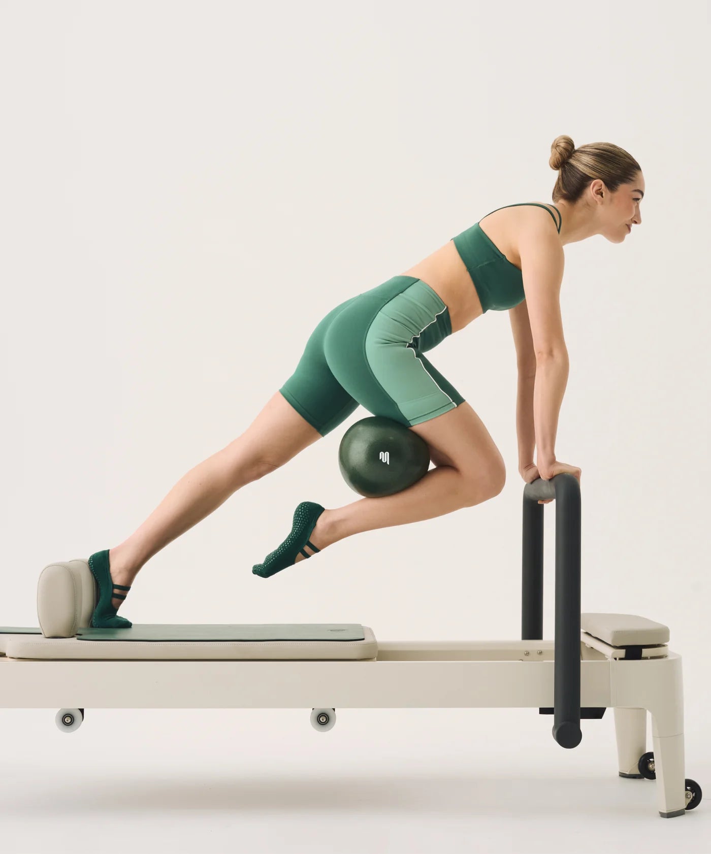 Woman exercising on a Pilates reformer machine with a pilates medicine ball.